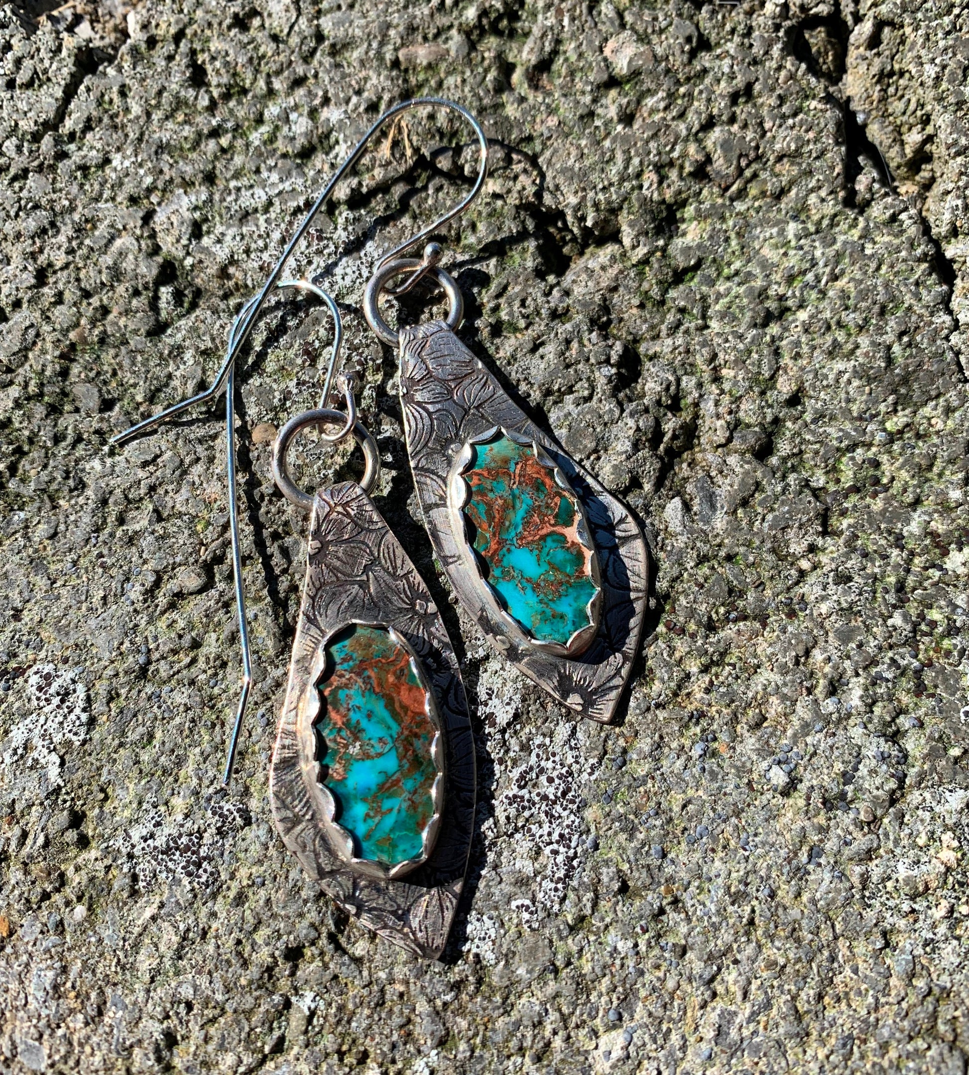 Pair of silver earrings with turquoise stone on a textured stone surface