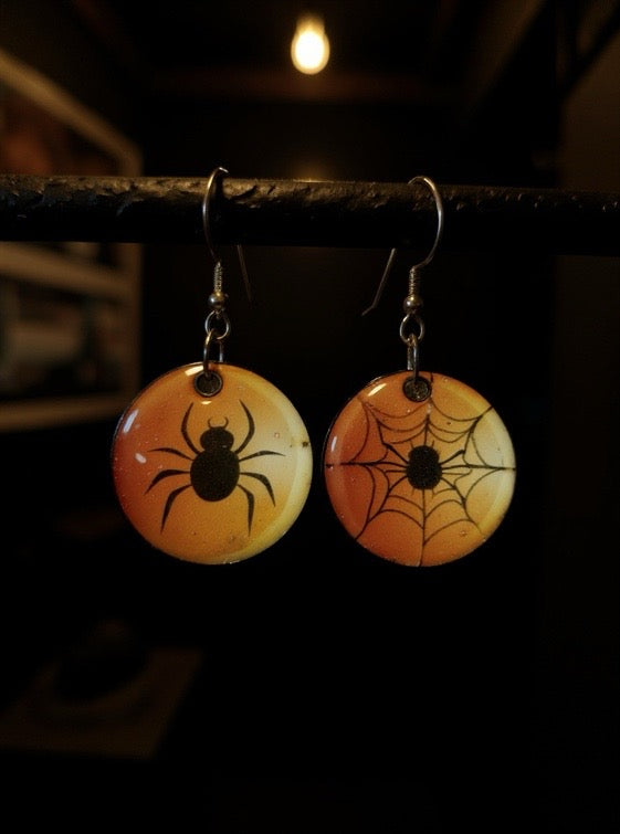Halloween-themed earrings with spider and web design on a dark background