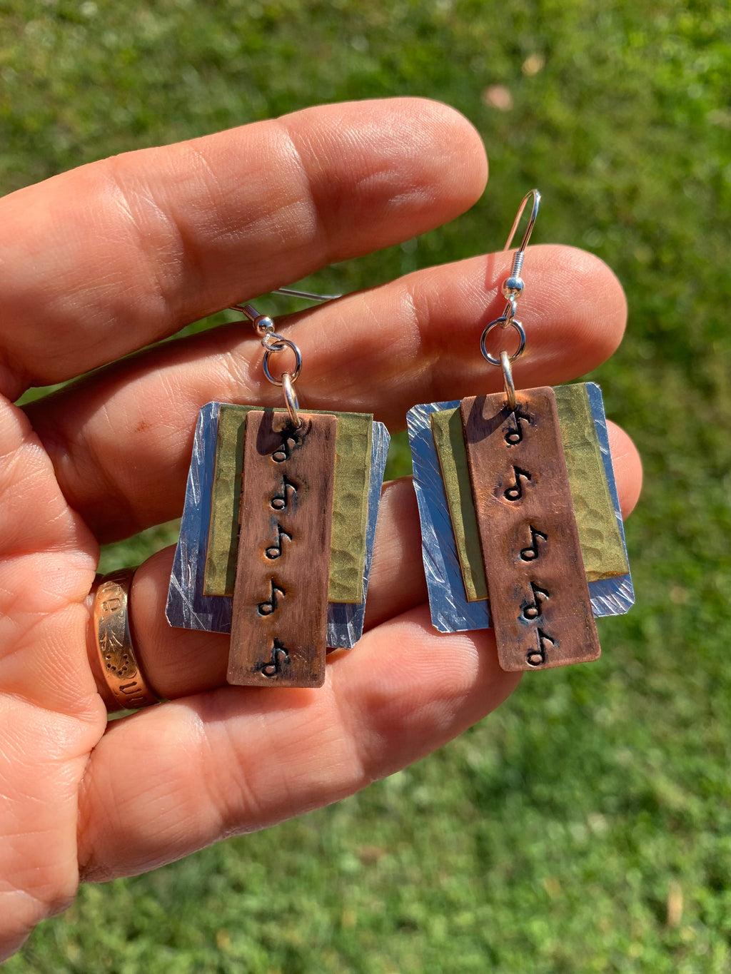 Hand holding a pair of earrings with musical note designs against a grassy background